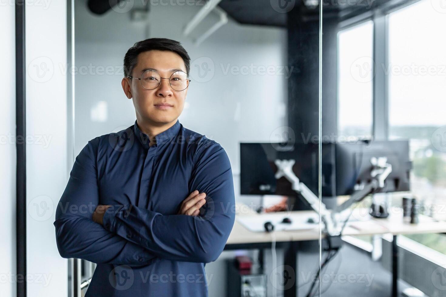 Portrait of businessman with arms crossed, asian man smiling and looking at camera, man working inside modern office building. photo