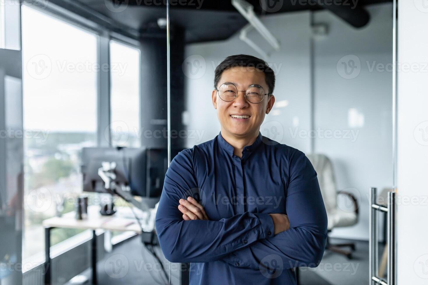Portrait of successful asian businessman with crossed arms, businessman investor working inside office building loft, looking at camera and smiling, satisfied investor financier. photo