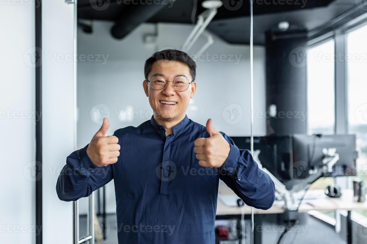 Portrait of successful asian businessman, man working in modern office looking at camera and smiling, broker trader showing thumbs up. photo