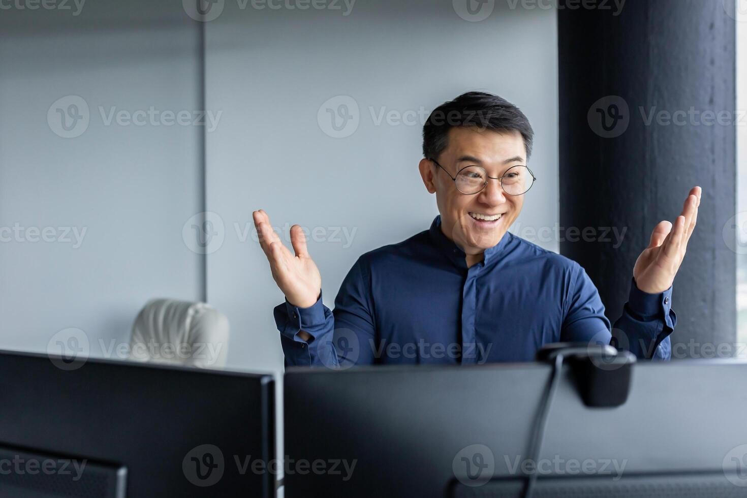 Online meeting with international partners. A happy young Asian businessman sits in a modern office at a table, communicates through a call. photo