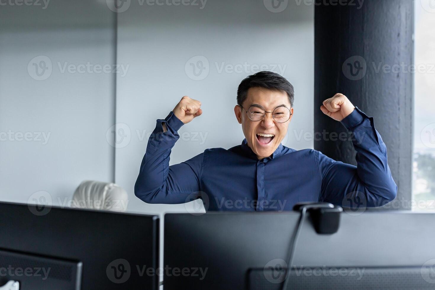 Happy Asian boss leader of programmer team, looking at computer screen and happy, celebrating victory, completed project, and submitted completed program, businessman entrepreneur holding hands up. photo
