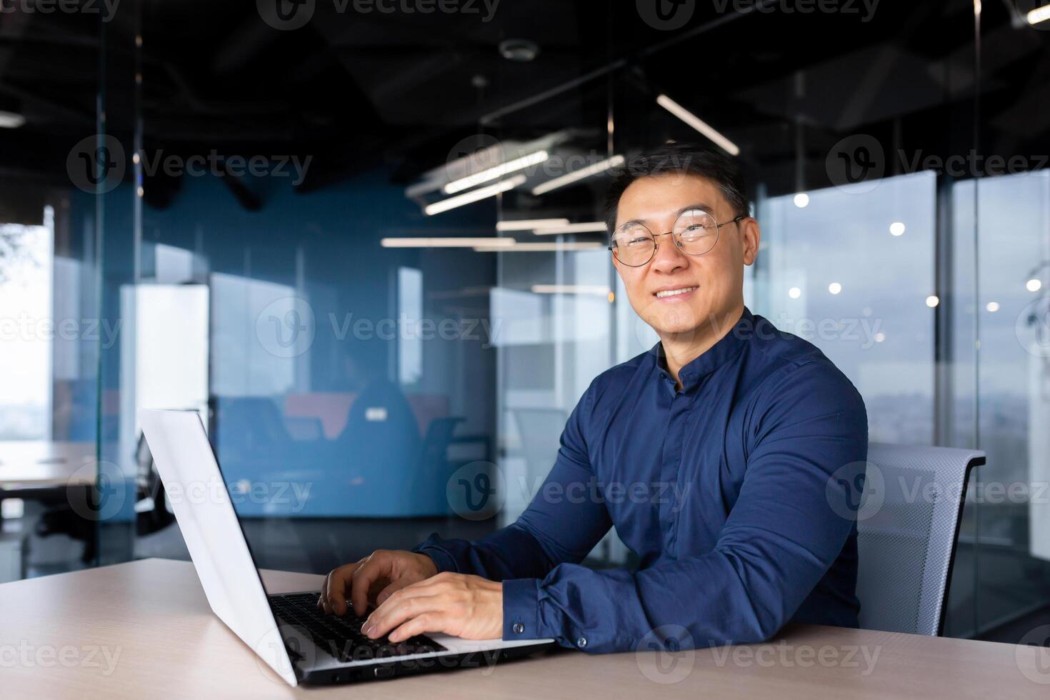 Successful asian businessman smiling and looking at camera, programmer porter inside office using laptop writing code for software security. photo