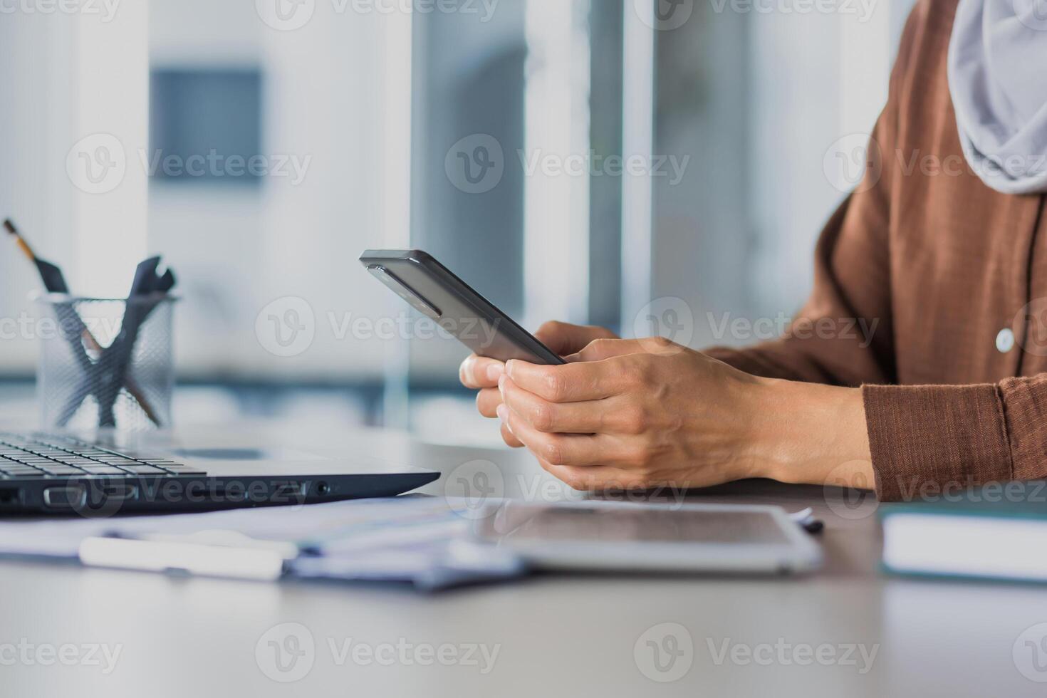 Close-up photo selective focus of business woman's hands typing on the phone, woman working at a table with documents and a laptop in a modern office