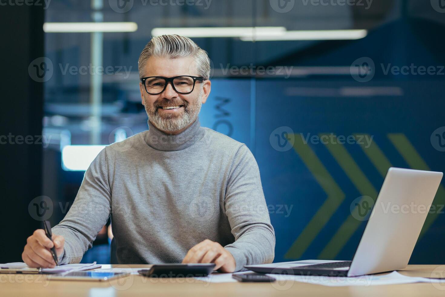 Portrait of successful senior businessman, gray haired man in glasses smiling and looking at camera, mature investor boss working inside modern office building using laptop at work. photo