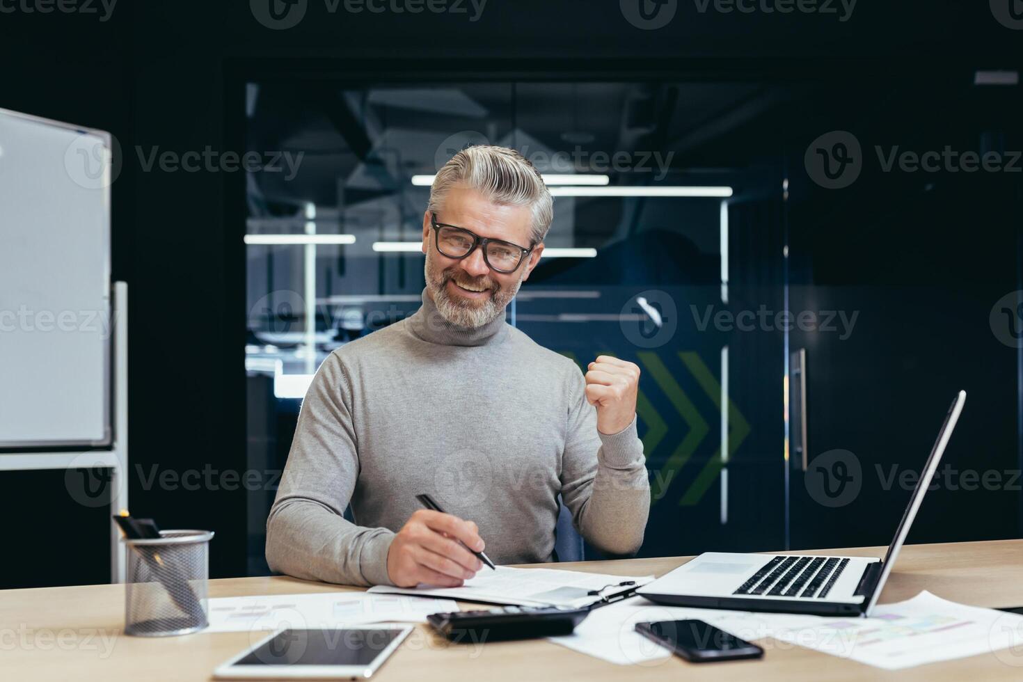 Portrait of successful mature financier, senior gray-haired man looking at camera and smiling, businessman in glasses paper work on reports and deals, using calculator and notebook in office. photo