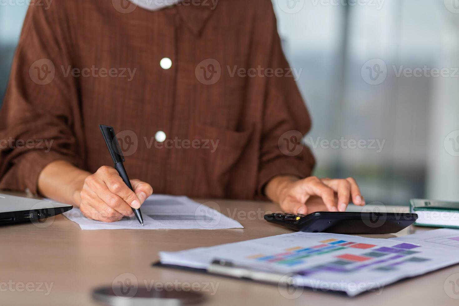 Close-up photo. Female hands of an accountant, auditor, financier, banker working in the office at a table with documents and with a laptop, using a calculator. photo