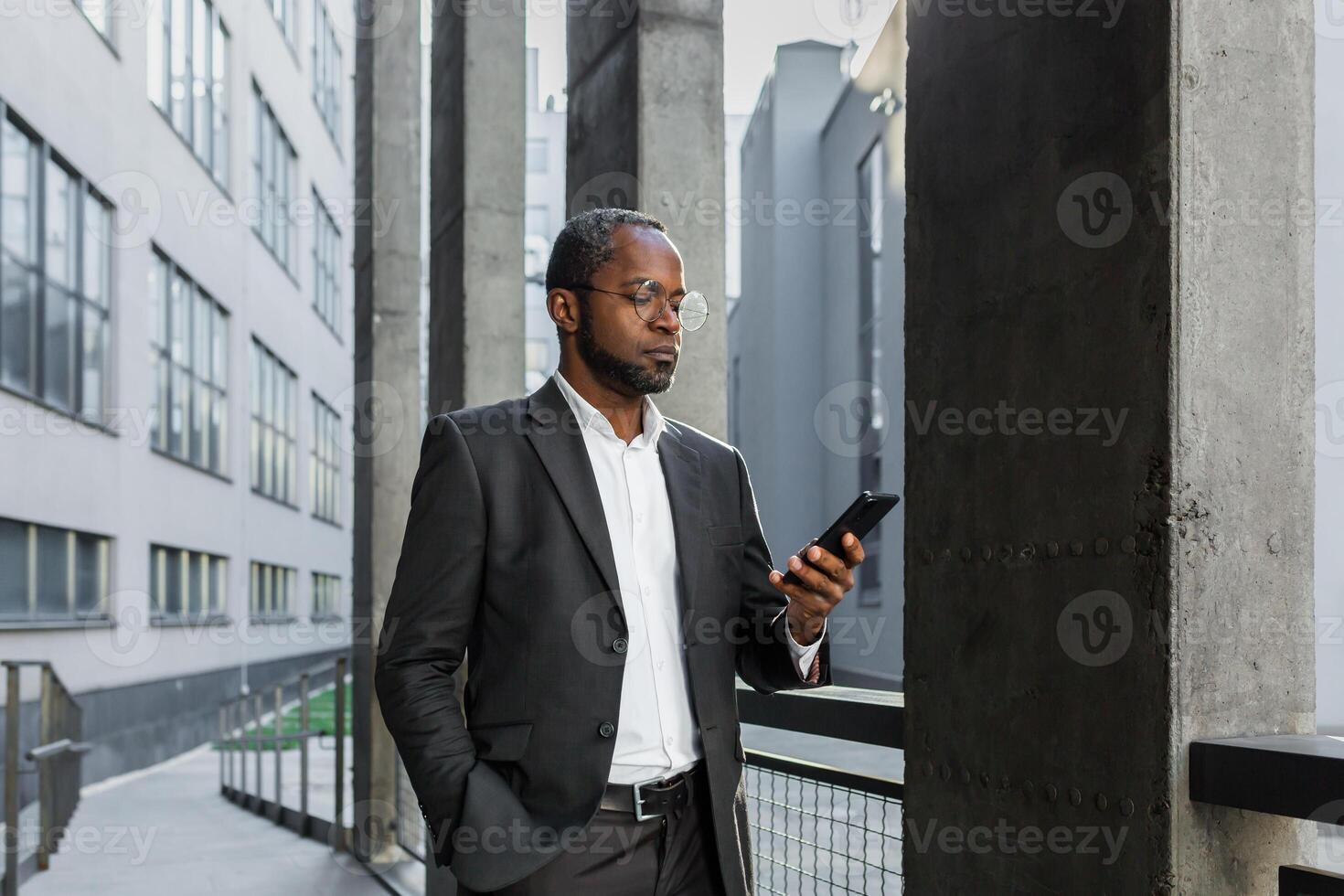 Serious and successful African American boss businessman outside office building using smartphone, man in business suit reading news online thinking and browsing internet pages. photo