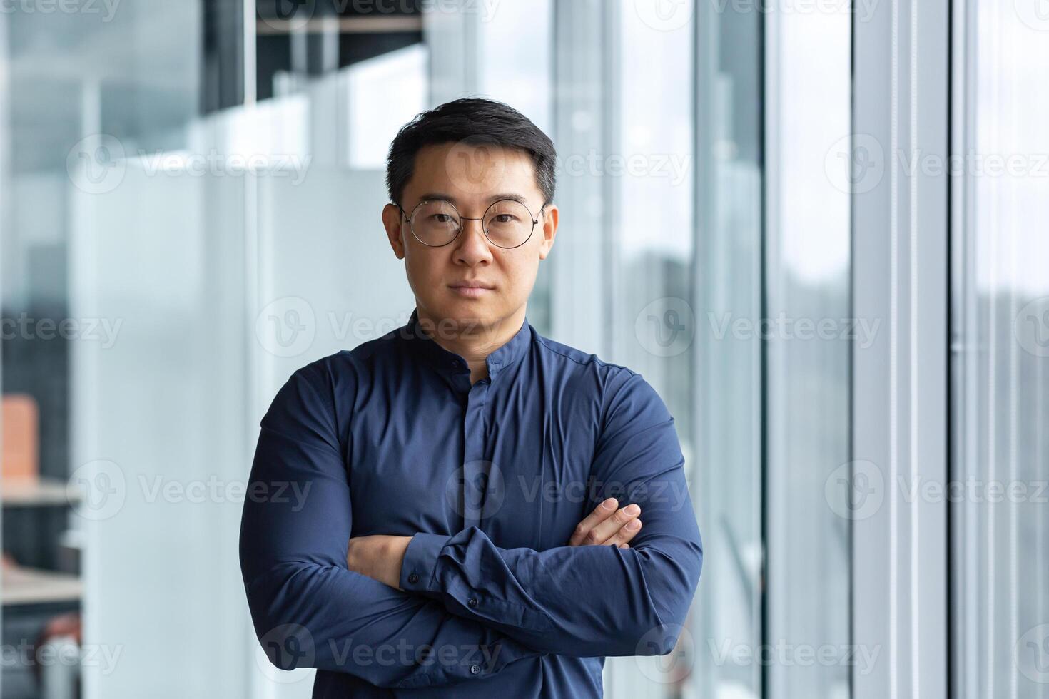 Portrait of successful and serious asian boss in shirt, man looking at camera with crossed arms inside modern office building near window. photo