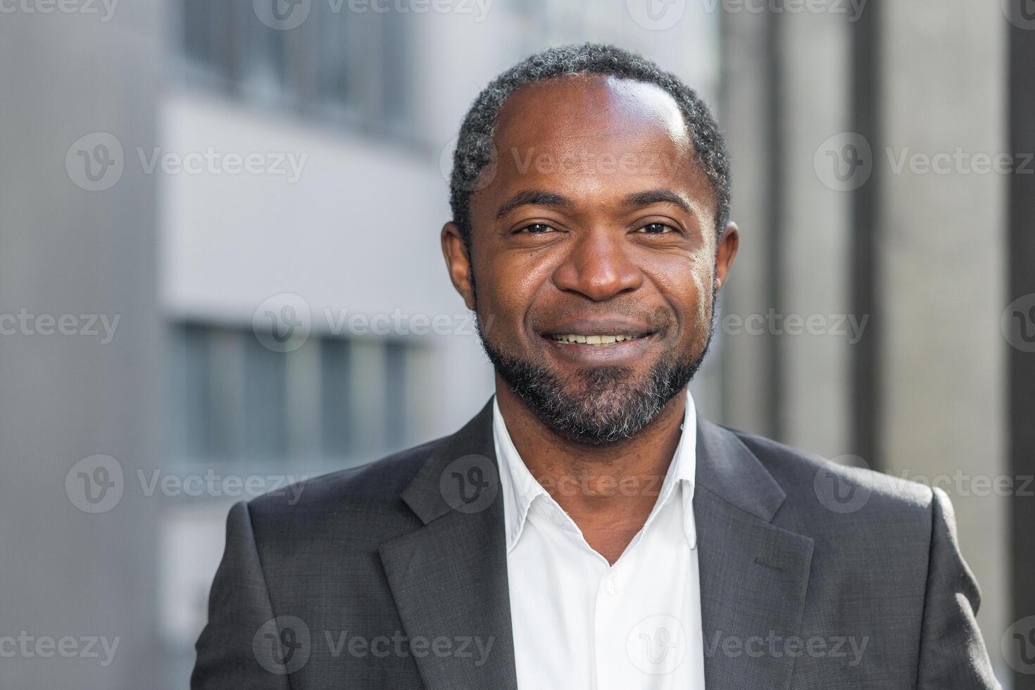 African american businessman close up, mature man smiling and looking at camera, senior boss in business suit portrait, outside modern office building. photo