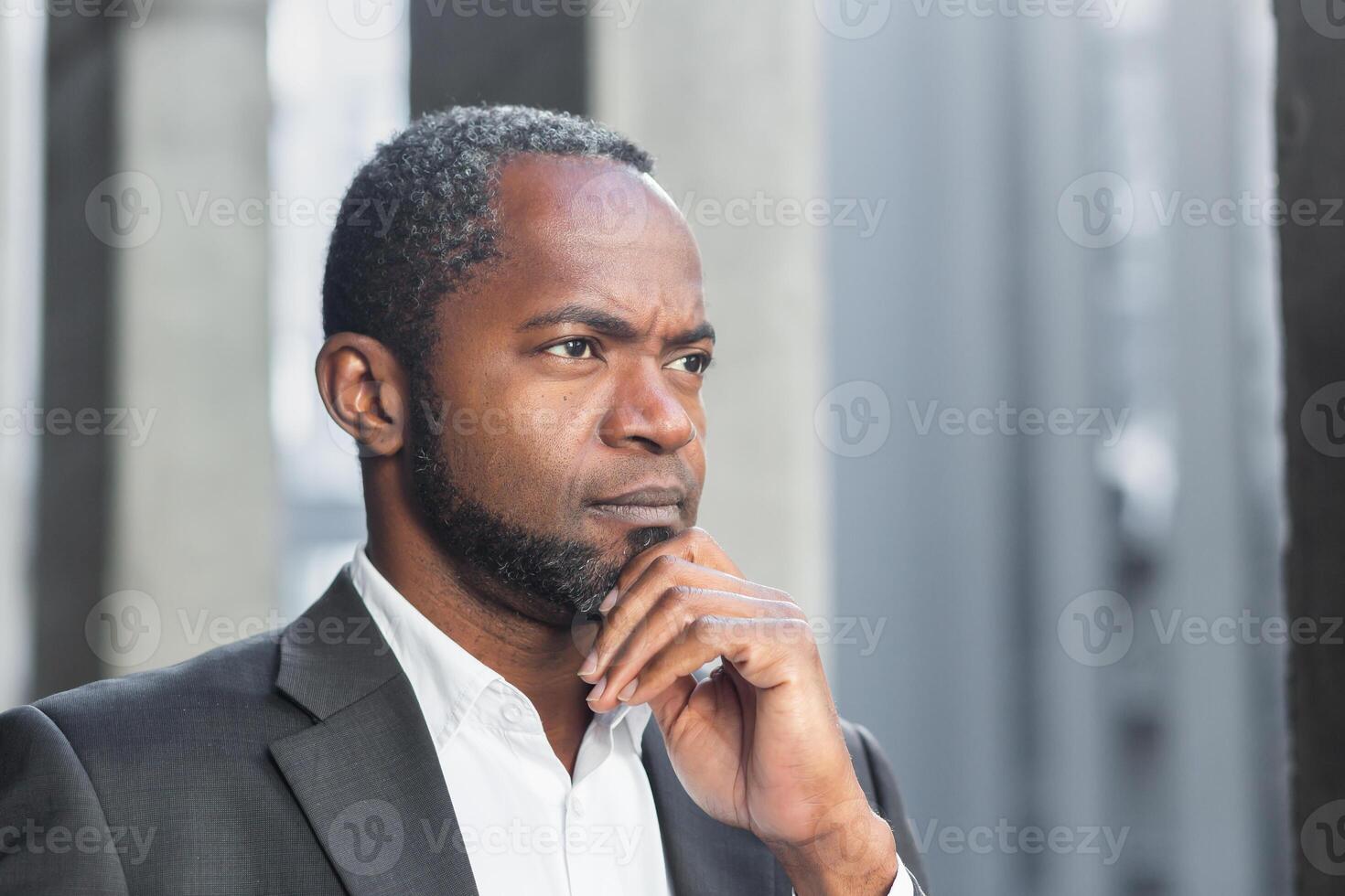 Close-up photo. Portrait of African American businessman, lawyer, right defender. He is standing in a suit near the courthouse, thoughtfully holding his hand on his chin, looking to the side. photo