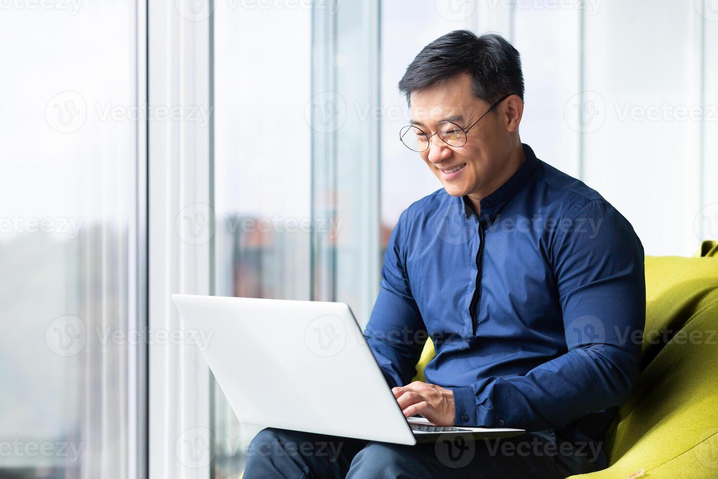 Successful and smiling asian man working with laptop inside office with notebook, senior businessman in glasses and shirt. photo