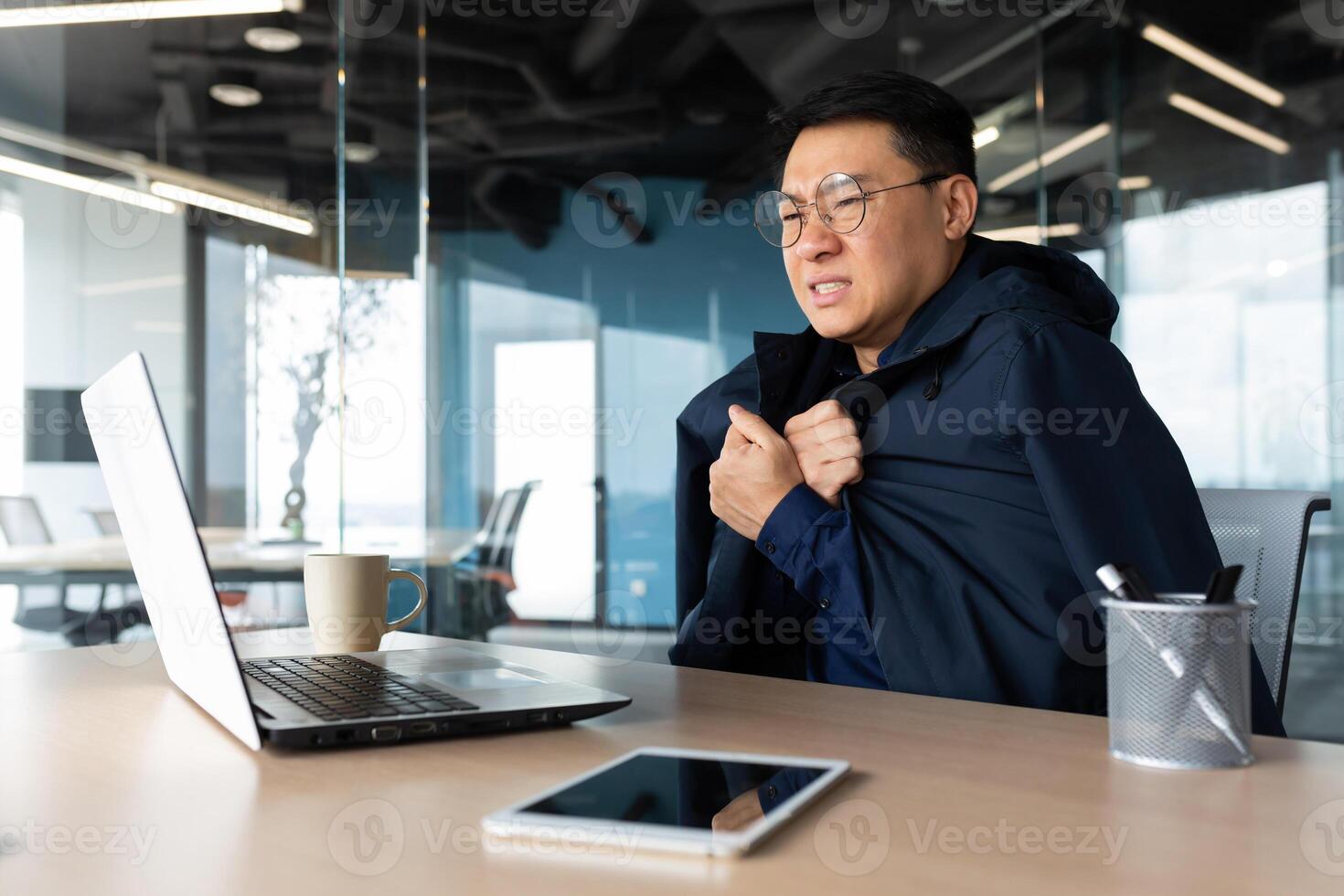 There is no heating in the office and the heater is broken, the businessman is freezing at the workplace, the man is sitting at the table inside the building using a laptop at work. photo