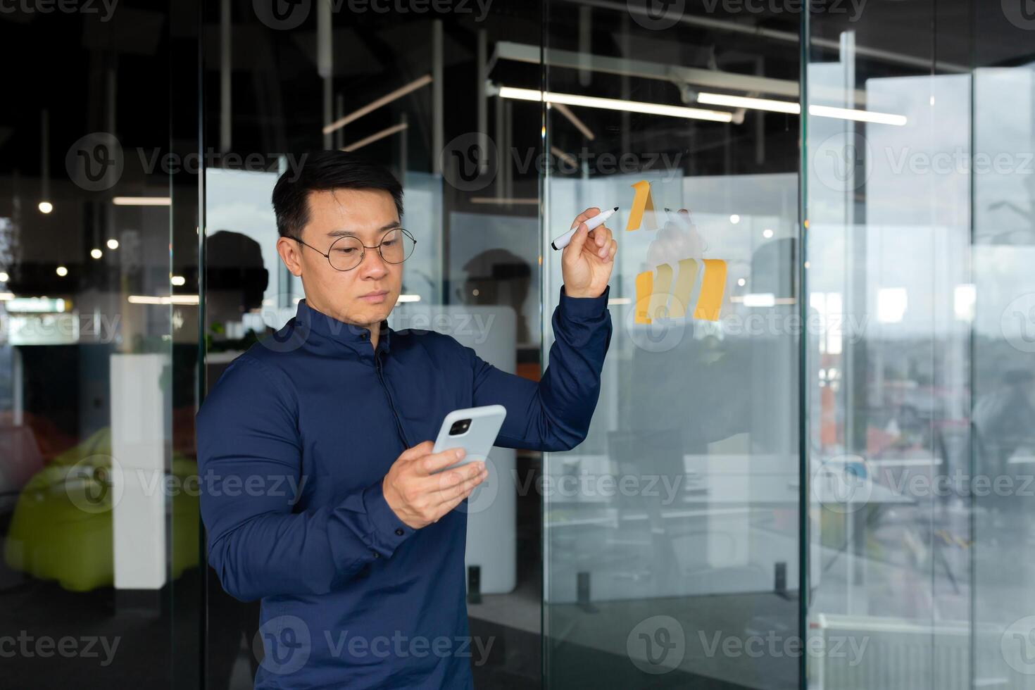 Asian man in thought writing down plans and strategy on colored paper on glass board, brainstorming in businessman at work. photo