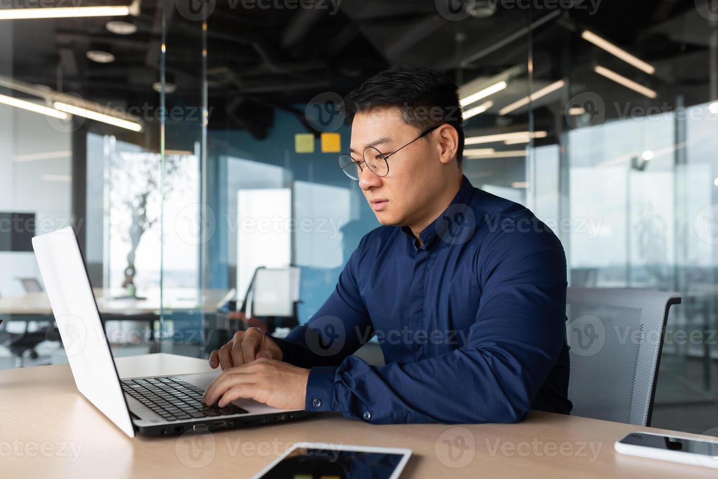 Serious and thoughtful businessman working inside office sitting at table using laptop at work, mature asian boss in shirt thinking and typing on keyboard. photo