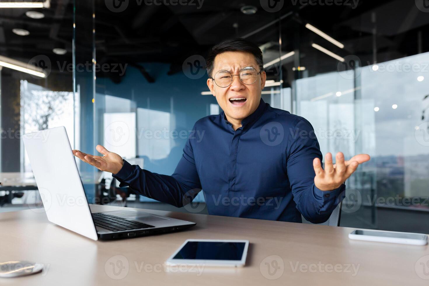 Portrait of frustrated and angry boss inside office, asian man looking at camera and shouting upset, man at workplace using laptop unhappy with work result. photo