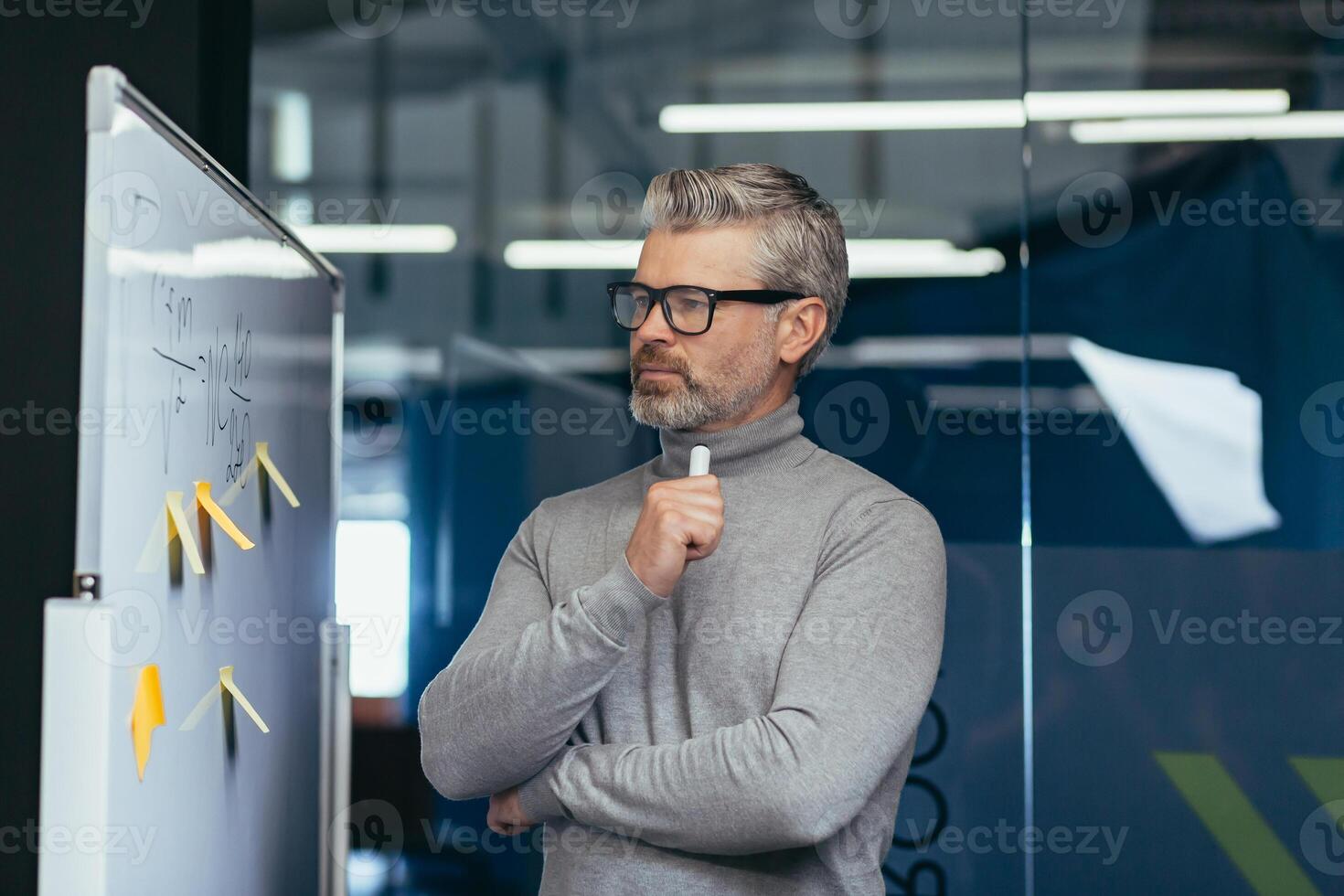 Thinking man inside the office near a white board with stickers, a businessman thinks about the plan and strategy of the company's finances, a gray-haired boss at work. photo