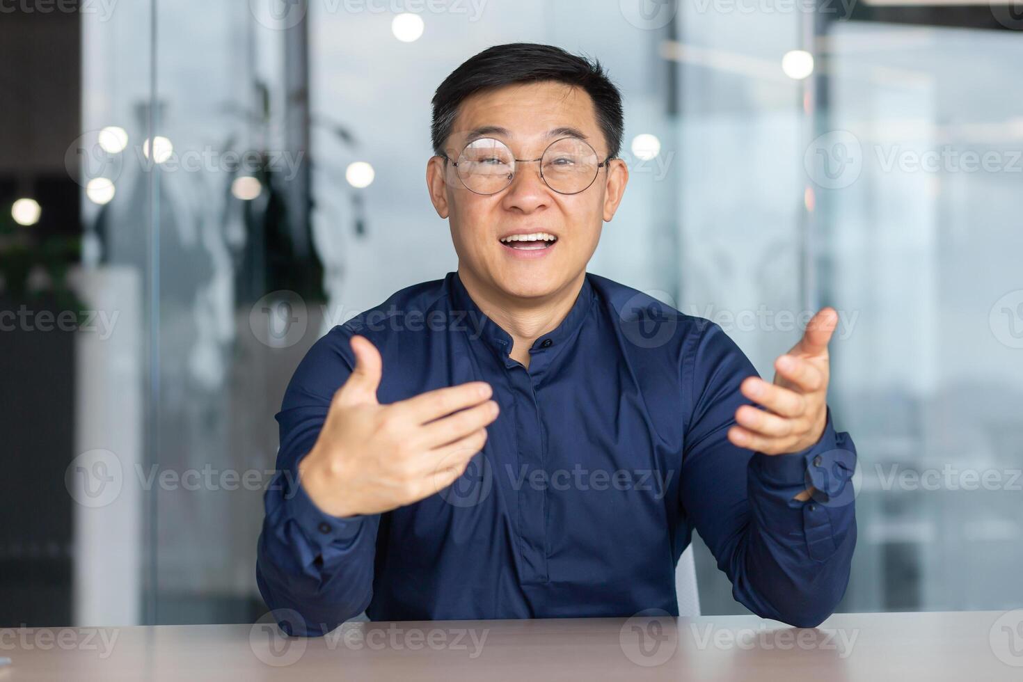 call online meeting asian businessman looking web camera and having fun talking and gesturing, man working inside office sharing plans with partners and colleagues, boss in shirt and glasses. photo