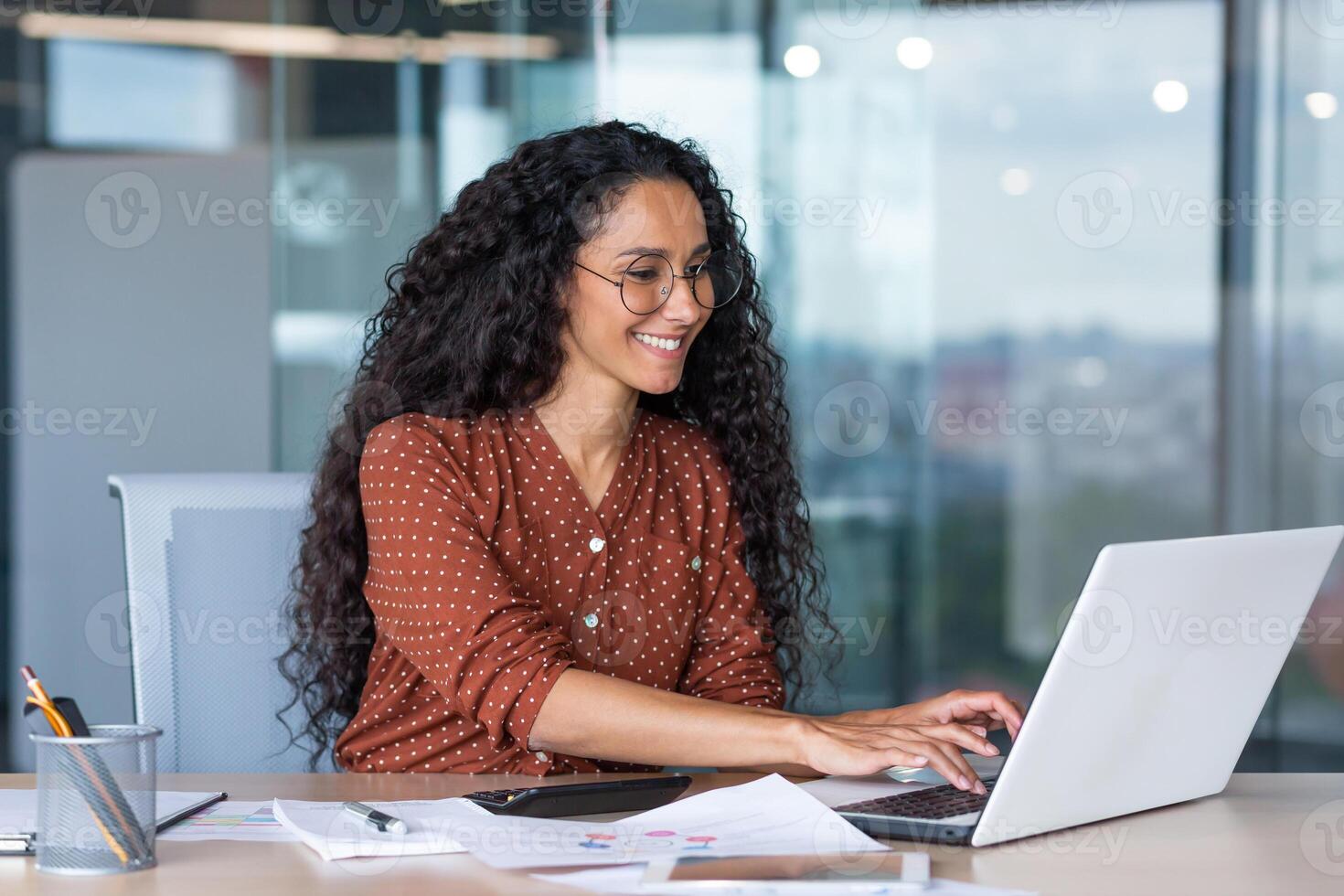 Online meeting. A young beautiful Latin American woman is sitting in the office at a desk, talking on a call from a laptop. Working meeting, webinar, online conference photo