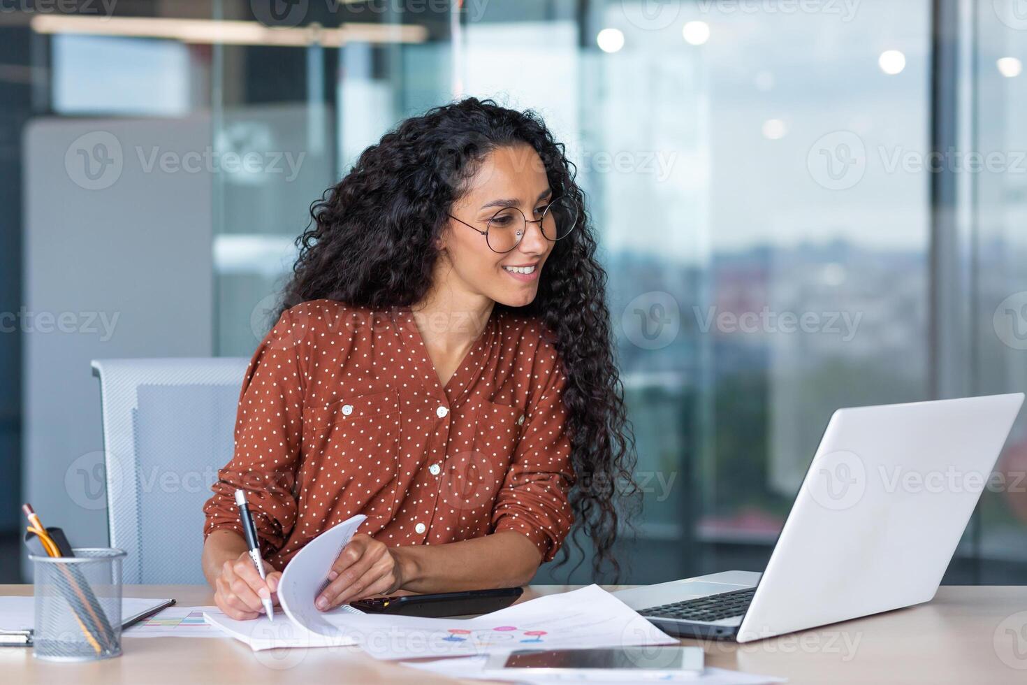 latin american businesswoman working inside office with documents and laptop, worker paperwork calculates financial indicators smiling and happy with success and results of achievement and work photo