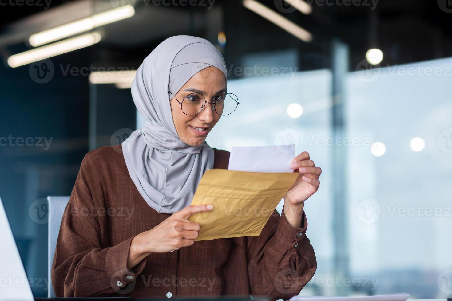 A young happy Arab female student in hijab. Sitting at the desk in the office, holding an envelope with a letter, he received a notification of admission to the university, the results of the exams. photo