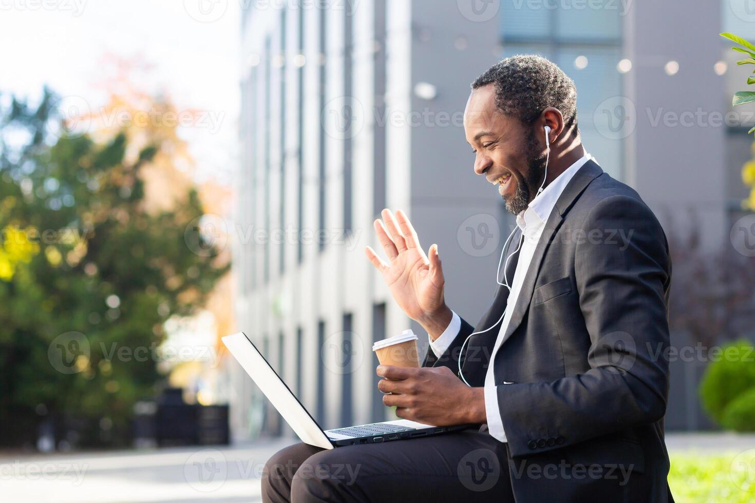 call of successful and happy African American businessman, man outside office building with headset talking to colleagues and partners, online meeting using laptop, boss in business suit. photo