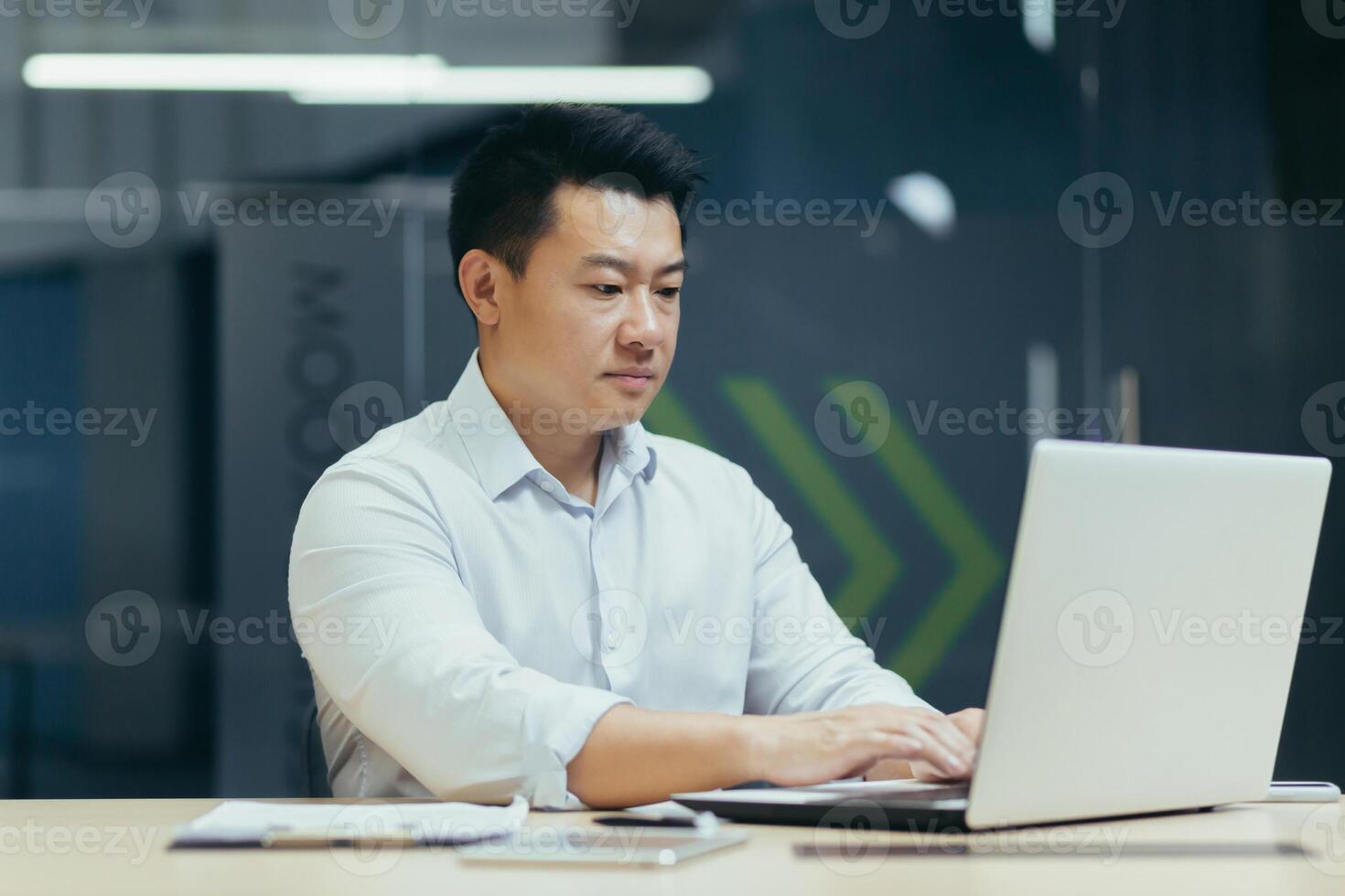 A young man of Asian origin programmer, developer works in the office at a desktop using a laptop. photo