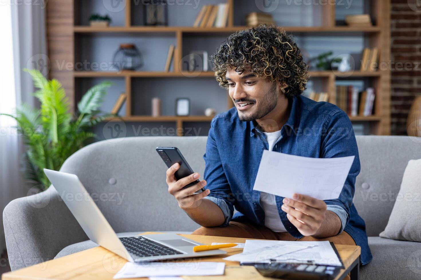 Happy man using smartphone and laptop for online bill payment at home photo