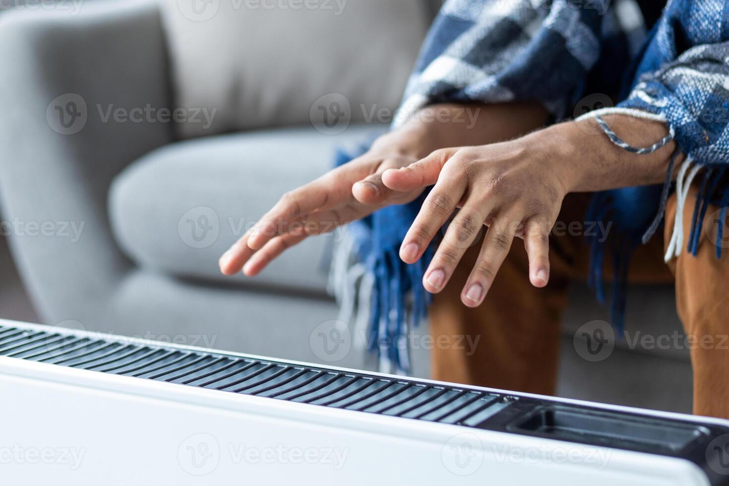 Man hands close up near a heating device. Man tries to warm himself while sitting at home on a sofa in the living room, there is no heating in the apartment photo