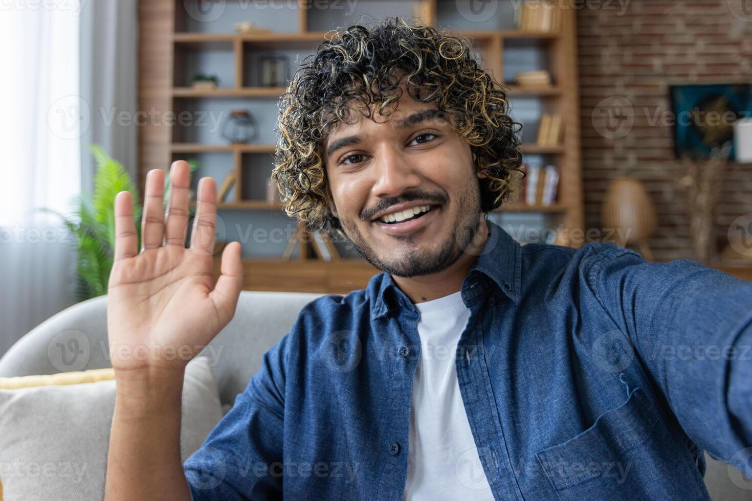 A man looks into the phone camera, happily waves his hand, takes a selfie photo and talks to colleagues and friends remotely using a smartphone app for chats
