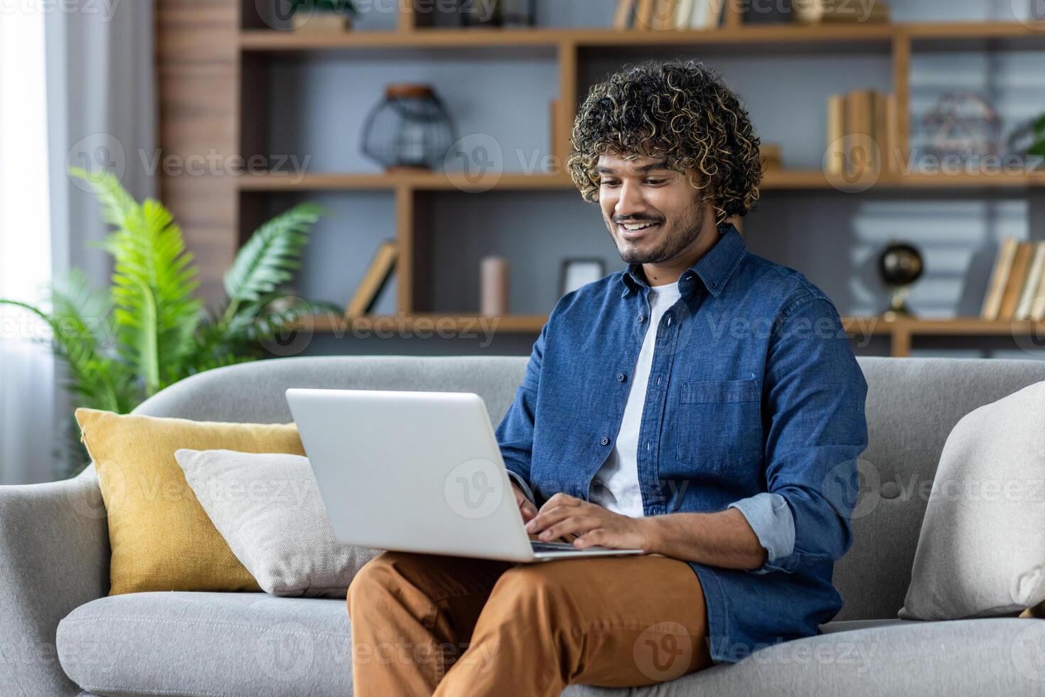 Smiling man using a laptop while sitting on a comfortable couch at home photo