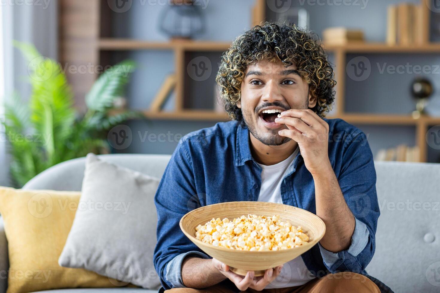 Man enjoying a bowl of popcorn while relaxing on the sofa at home photo