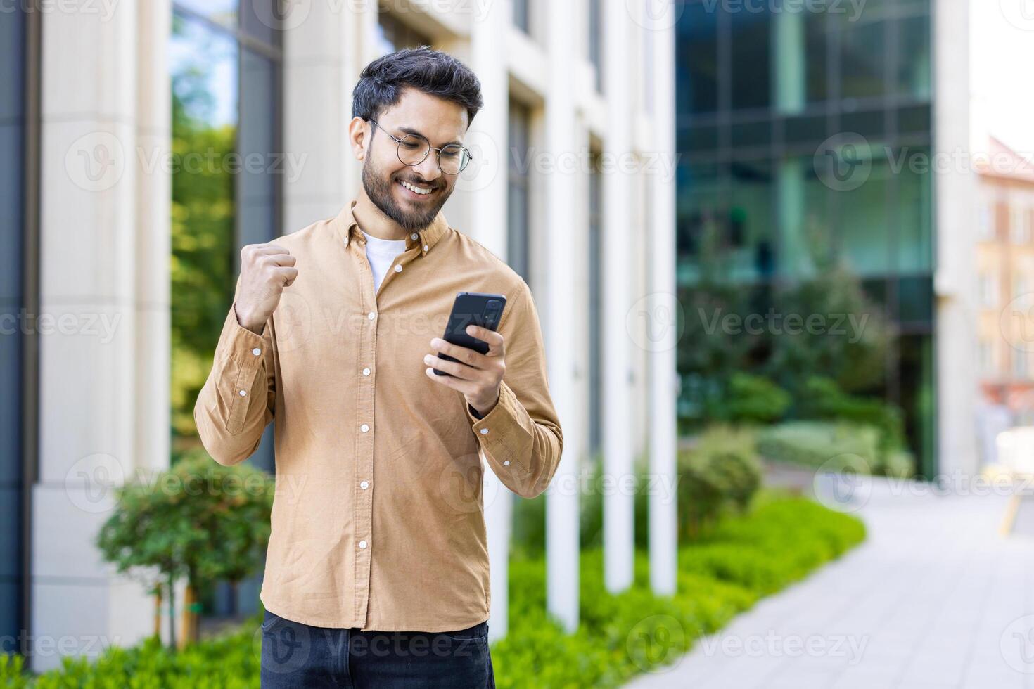 Man celebrating success while looking at smartphone outside modern office building photo
