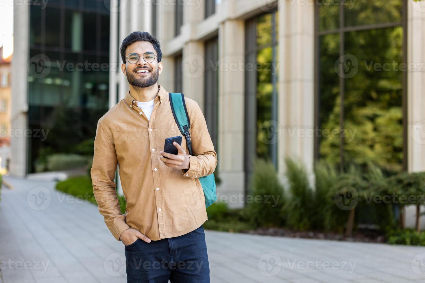 Smiling young student holding smartphone outdoors on a university campus photo
