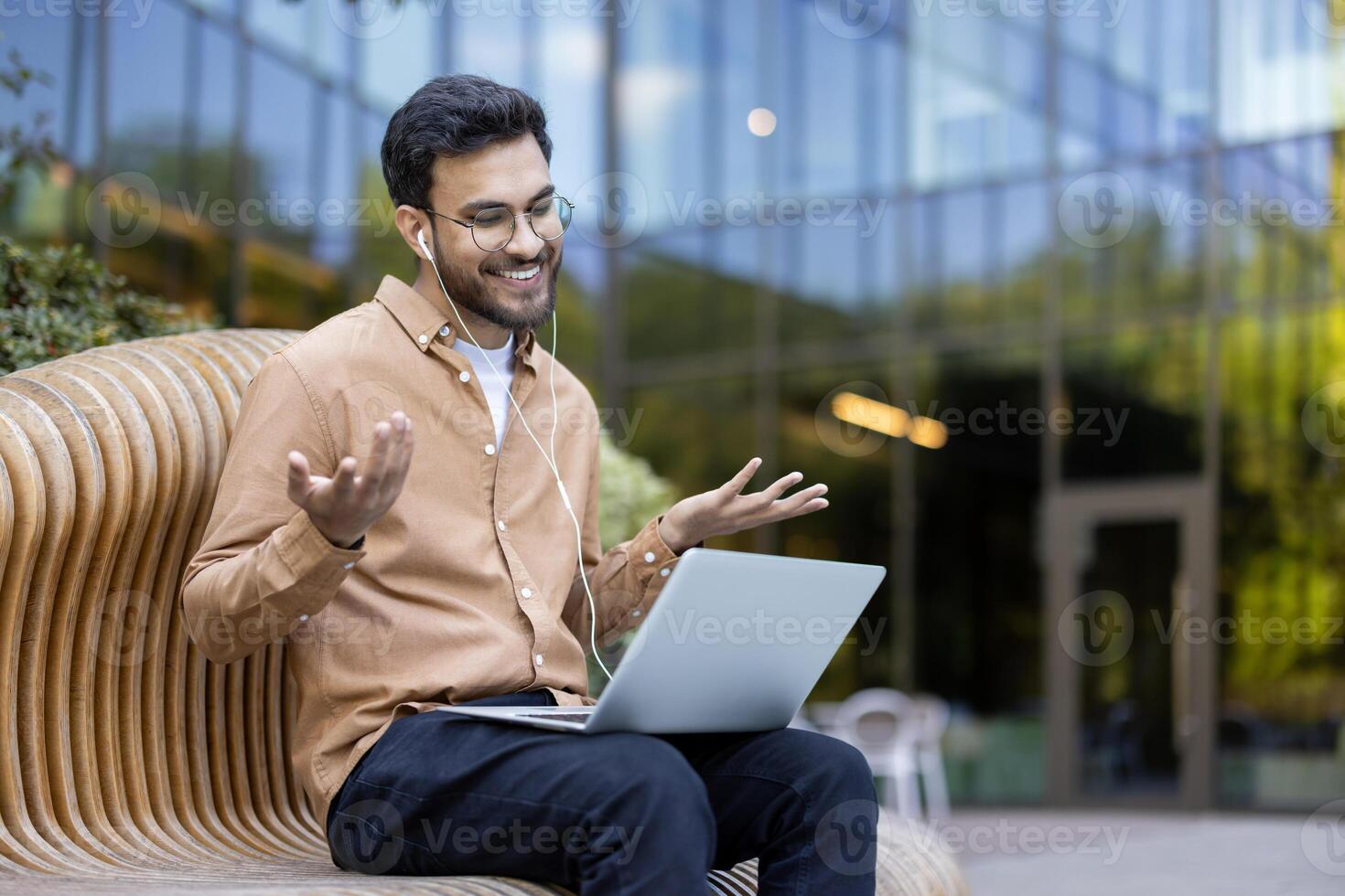 Young professional enjoys a call outdoors using laptop and earphones with an office building in the background reflecting the lively urban environment photo