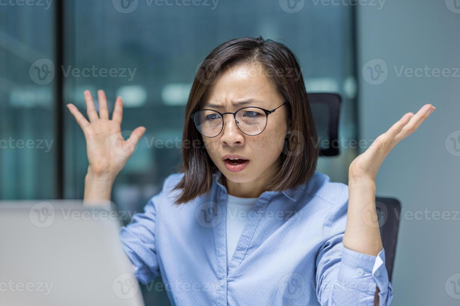 An Asian woman stares in disbelief at her computer screen in the office, experiencing frustration with an error or unexpected outcome. photo