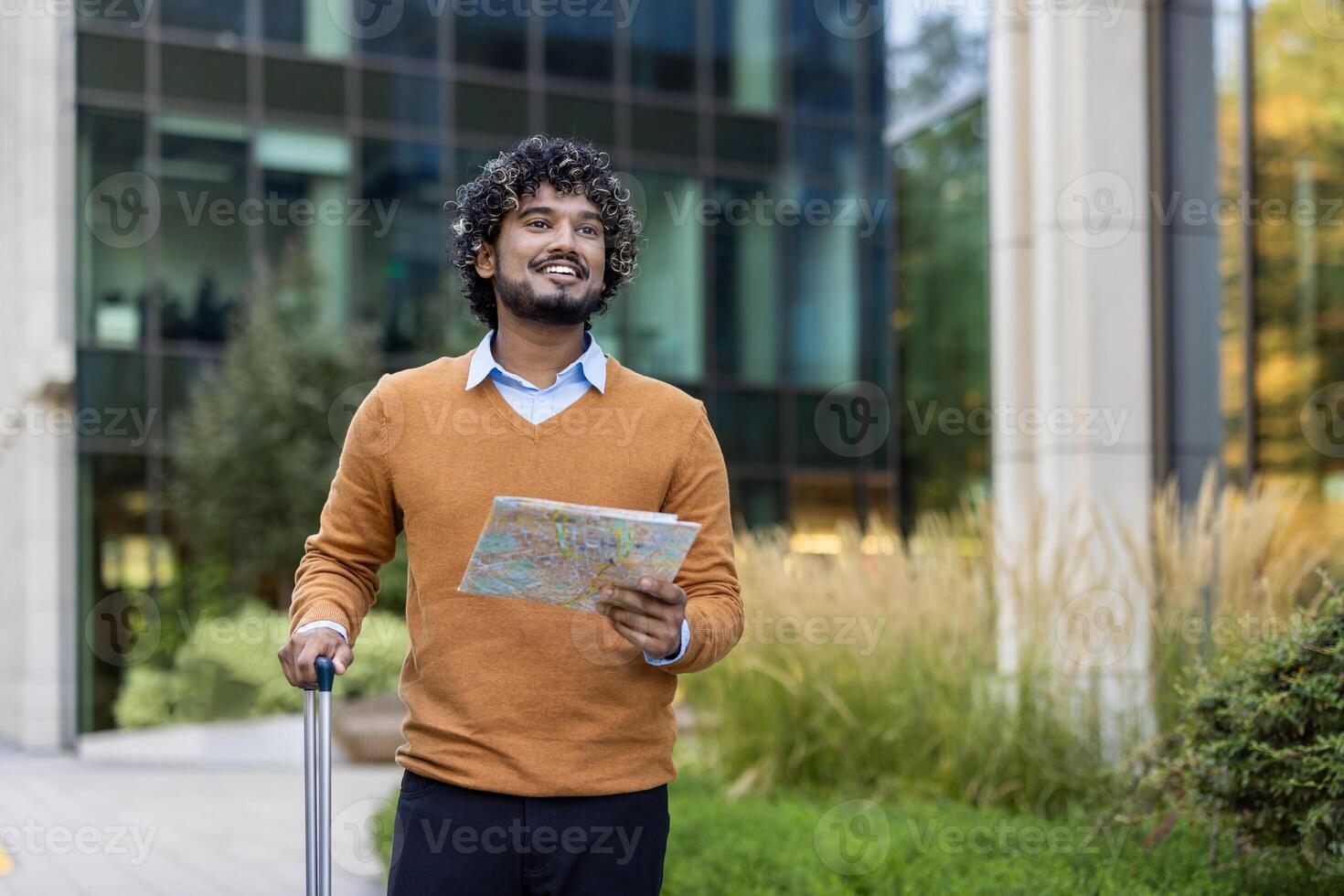 Young businessman holding map and suitcase outside modern office building. He looks ready to embark on travel journey, exuding confidence and curiosity. Perfect portrayal of urban exploration. photo