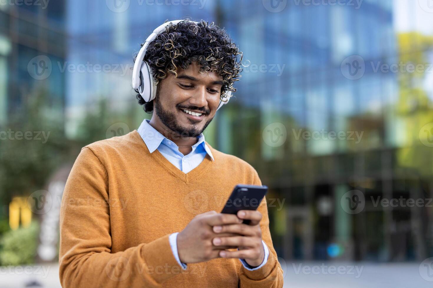 Smiling young man using smartphone with headphones in urban environment. Image captures casual lifestyle, technology interaction, and modern communication. photo
