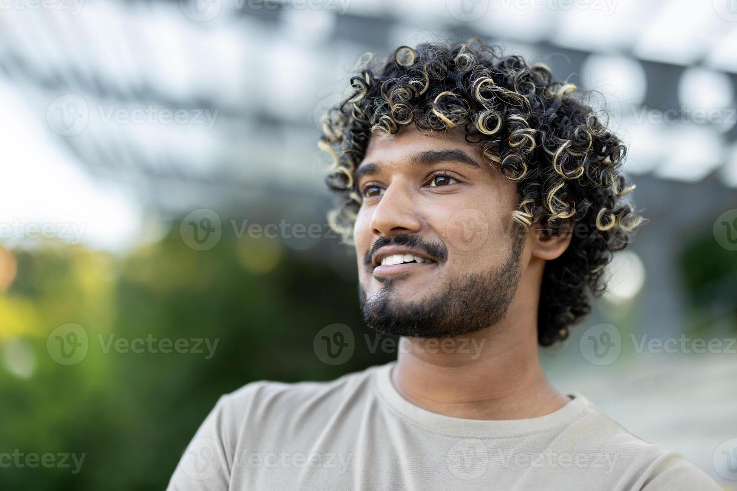 Young happy man with close-up smiling and looking to the side, wearing a t-shirt walking through the city and park. photo