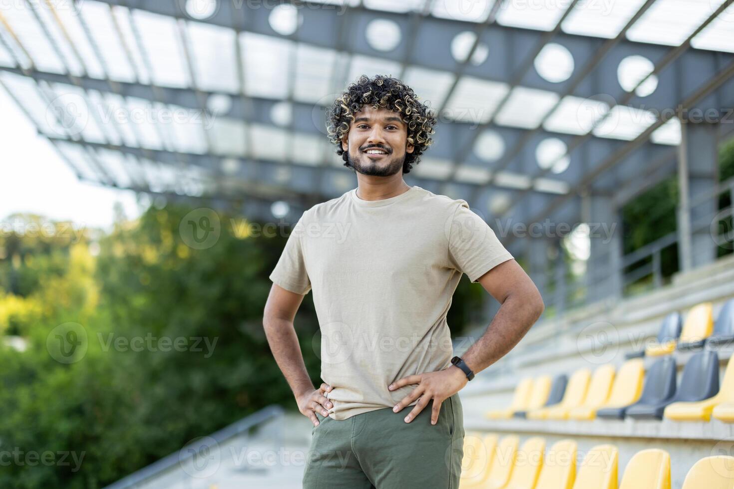 Young man with curly hair confidently stands at a stadium, ready for his fitness and exercise routine outdoors. photo