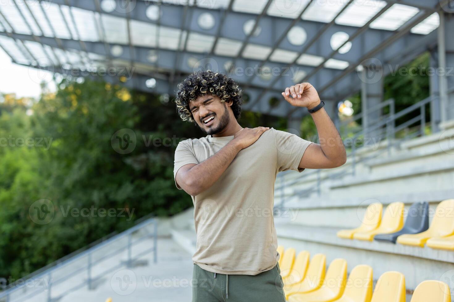 The athlete was injured while engaging in active physical exercises and fitness. The man is massaging the shoulder and back muscles, standing outside in a park photo