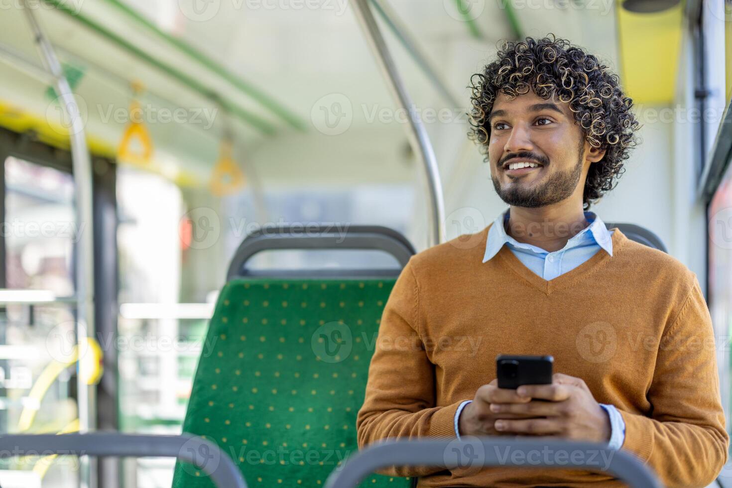 Happy man with phone in hands rides in public transport, passenger smiles and looks out the window, uses smartphone app to browse social media. photo