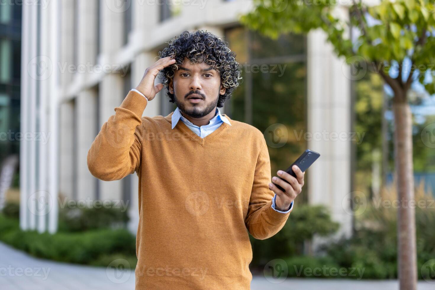 Young man outdoors holding phone expressing surprise. Dressed in casual outfit, standing near modern building, engaged in phone conversation. Captures moment of shock or unexpected news during call. photo
