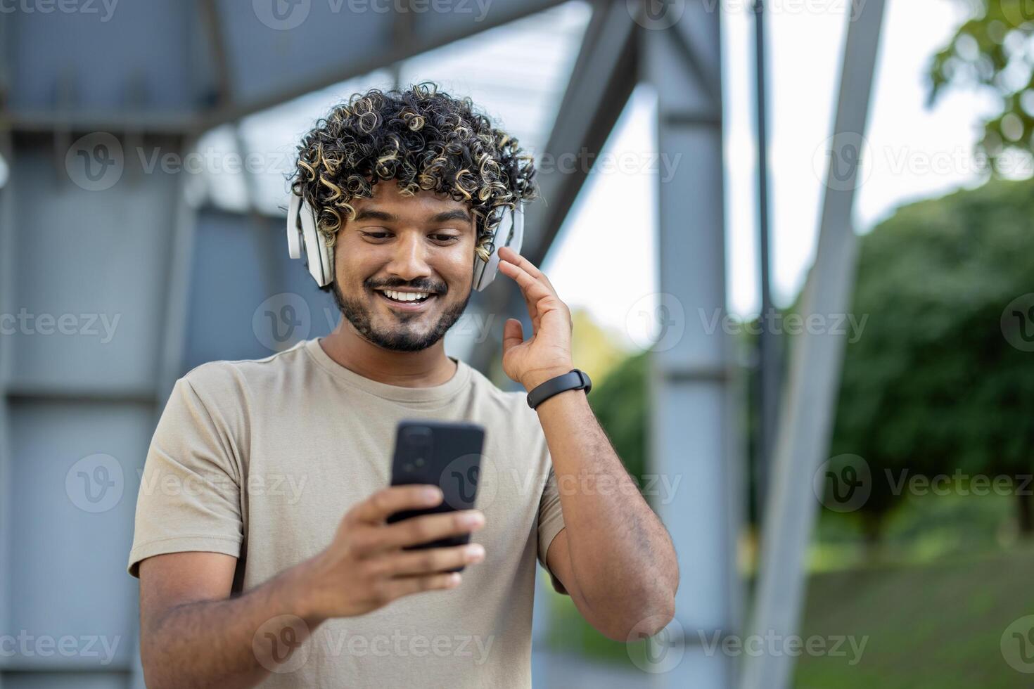 Young man in headphones and with phone listening to music and podcasts. Athlete resting during active physical exercise and fitness walking in the fresh air. photo