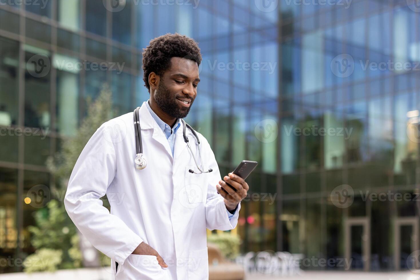 Successful doctor walking outside modern clinic office with phone in hand. Hospital worker using online app on smartphone, smiling contentedly. photo