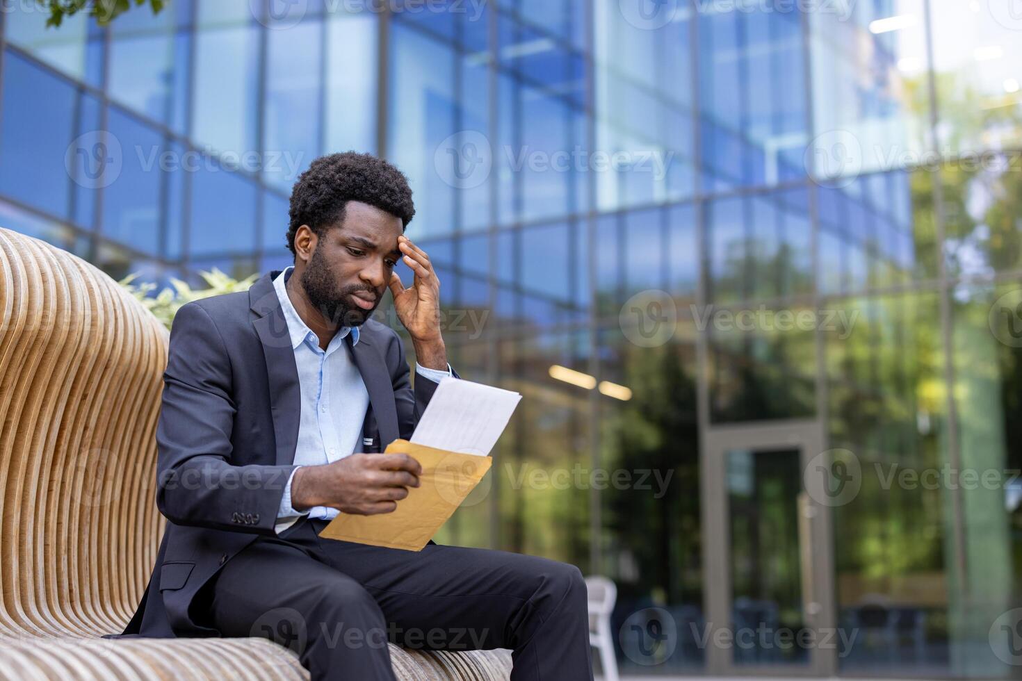 A young, formally dressed man looks worried as he reads a letter outside an office building, potentially facing bad news or challenges. photo