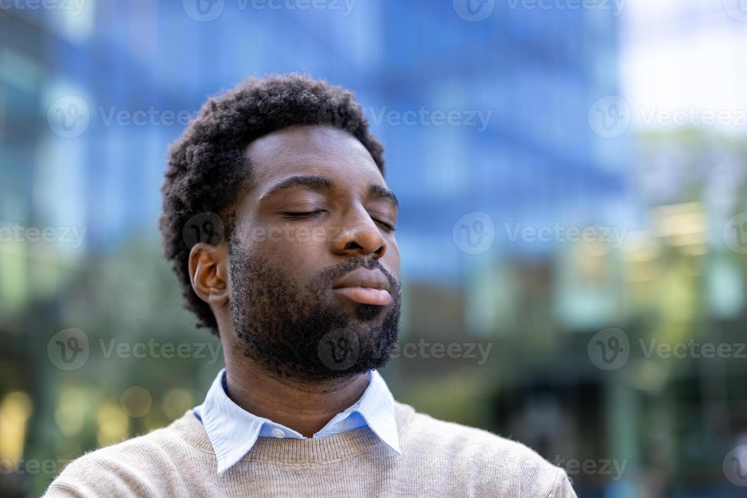 A serene portrait features a black man with closed eyes, emanating peace and mindfulness. He is dressed in a sweater, showcasing calm in a bustling urban environment. photo