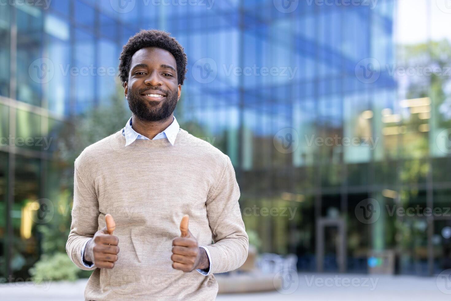 A smiling black man gives a thumbs up, standing in front of a modern building. The scene conveys approval and positivity. photo