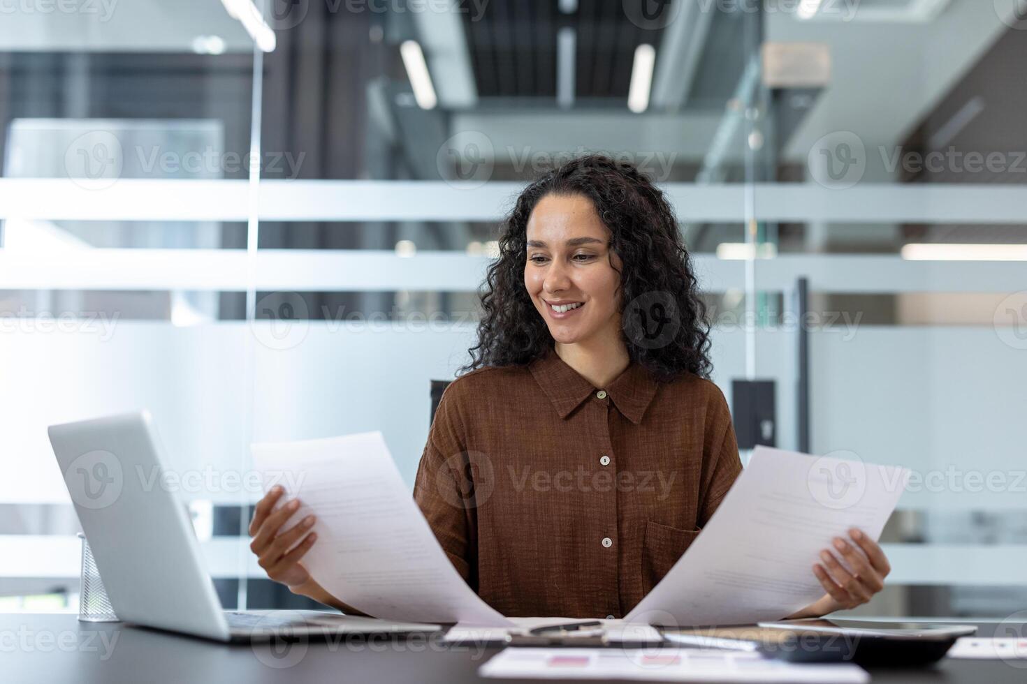 Successful joyful businesswoman doing paperwork, accountant smiling checking reports and tax forms. Woman reading data, sitting at desk with laptop. photo