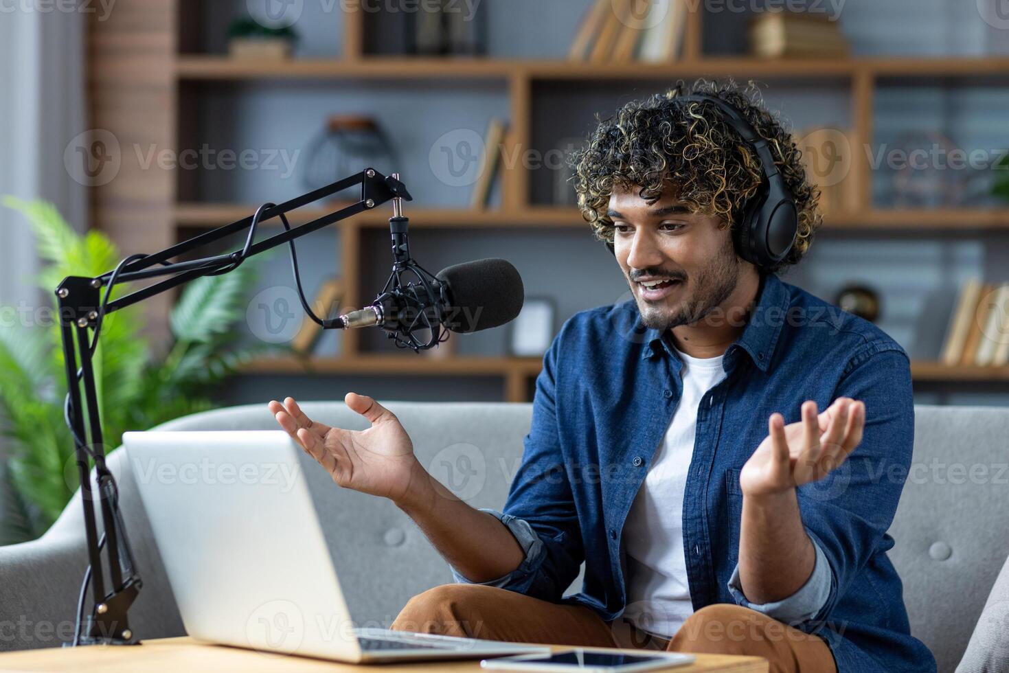 Young man enthusiastically records a podcast or participates in a lively online meeting from his living room, using a microphone and laptop. photo