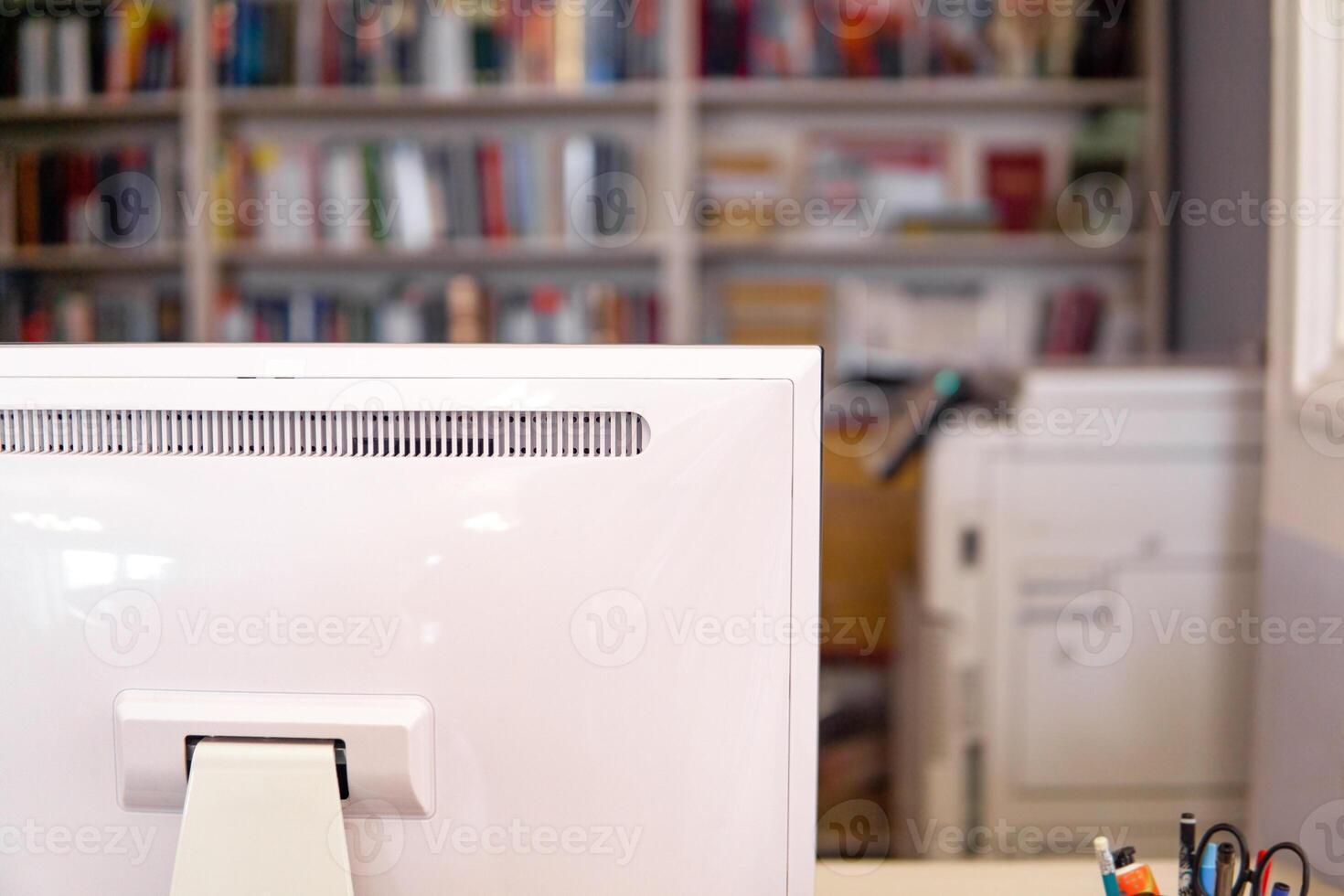 Close up of a white computer monitor in a library with bookshelf in the background photo